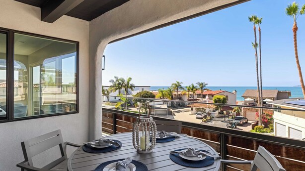 A balcony with a table set for dining, overlooking a coastal area with palm trees and houses. - Rooftop w/ Hot Tub, Ocean Views 259 Trailhead Trestles 1 by Avantstay (San Clemente)