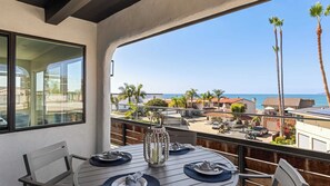 A balcony with a table set for dining, overlooking a coastal area with palm trees and houses. - Rooftop w/ Hot Tub, Ocean Views 259 Trailhead Trestles 1 by Avantstay (San Clemente)