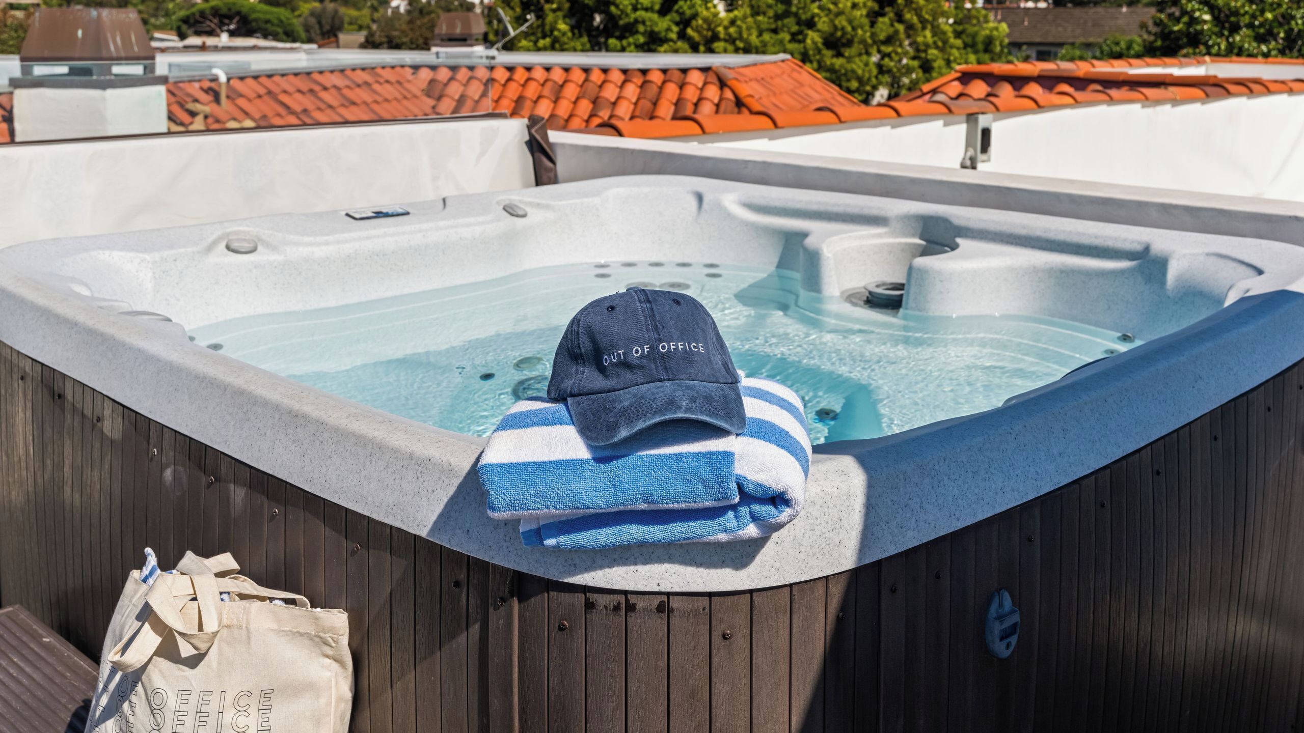 Un jacuzzi con una toalla y una gorra, una terraza de madera y una bolsa con la etiqueta 'FUERA DE OFICINA'.