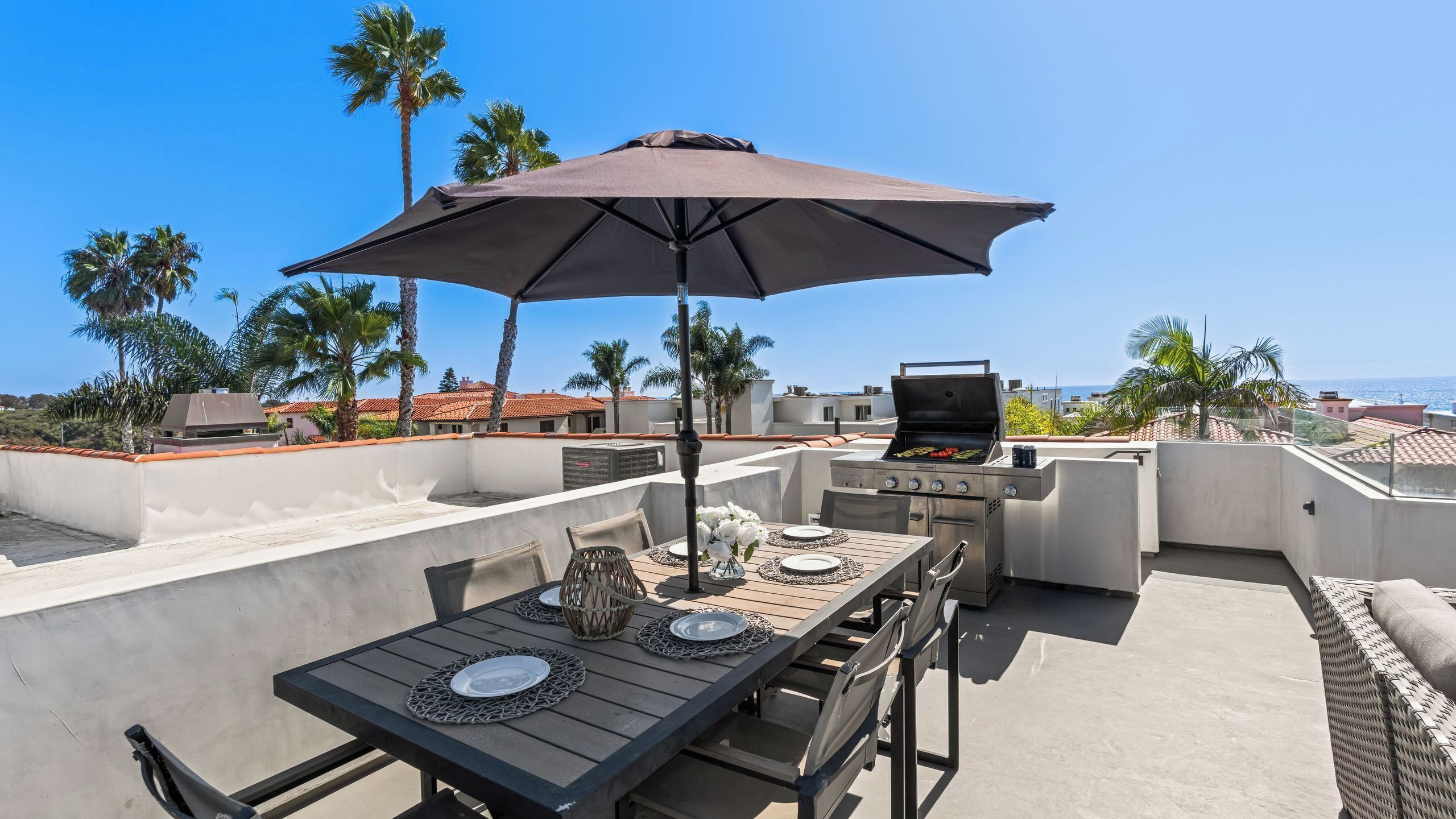 Un patio exterior con una mesa lista para comer, una parrilla y una sombrilla.