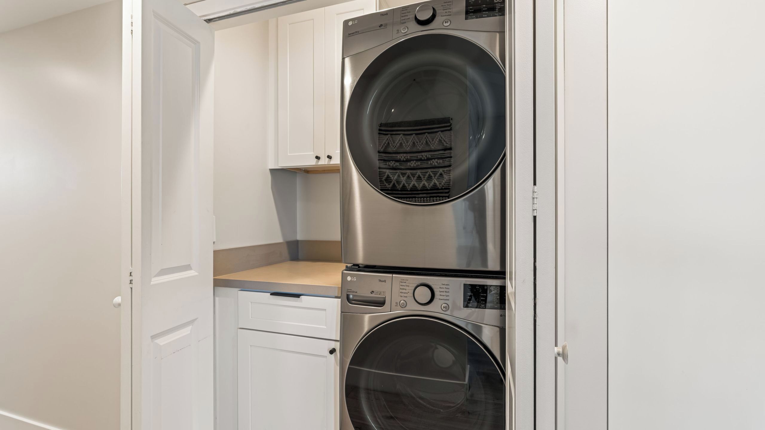 A laundry room with two stacked front-loading washing machines, a countertop, and a cabinet.