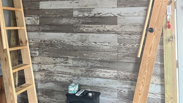 Una habitación con pared de madera rústica, un televisor plano montado, una escalera de madera y una estufa negra.
