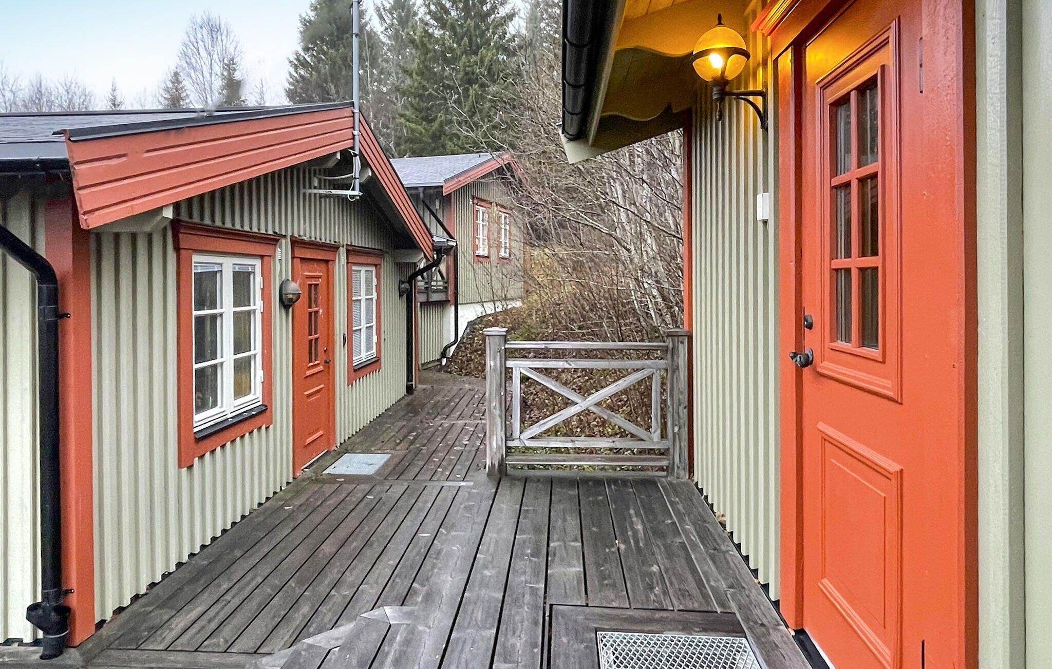 A wooden deck leading to a building with red and white exterior walls, a metal gate, and a small porch area.
