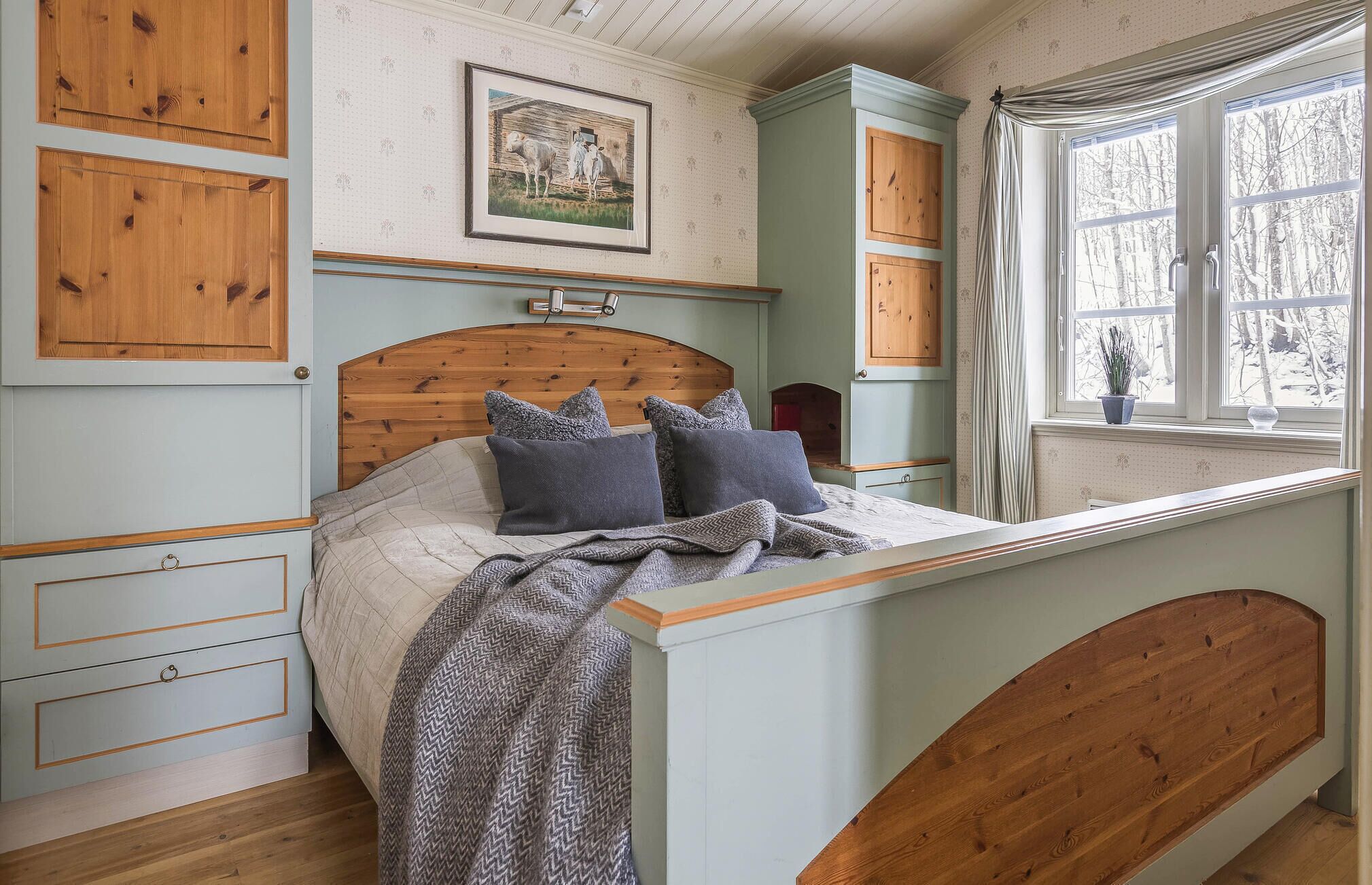 A bedroom with a wooden bed, a framed picture on the wall, and a window with curtains.