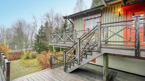 A wooden deck with a staircase leading to a building with a red door and a light fixture. - 2 bedroom beautiful apartment in åre (Åre)
