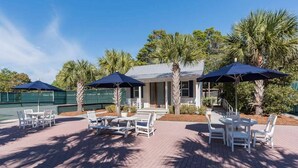 An outdoor patio area with white tables and chairs, shaded by blue umbrellas, and surrounded by palm trees. - Sunshine, Seaside and Nobellah's Retreat/ Pet Friendly/ 4 Bikes (Santa Rosa Beach)