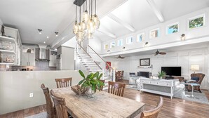 A spacious kitchen with white cabinets, a wooden dining table, and a staircase leading to a loft area. - Sunshine, Seaside and Nobellah's Retreat/ Pet Friendly/ 4 Bikes (Santa Rosa Beach)