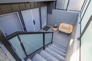 Un escalier menant à un palier doté d’une rambarde en verre, d’une chaise beige et d’une petite table ronde sur laquelle est posée une plante.