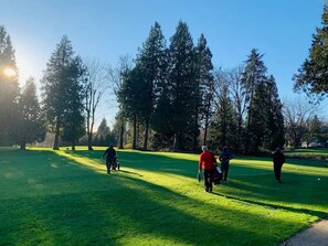 Un terrain de golf avec un ciel dégagé, des arbres et des gens qui se promènent.
