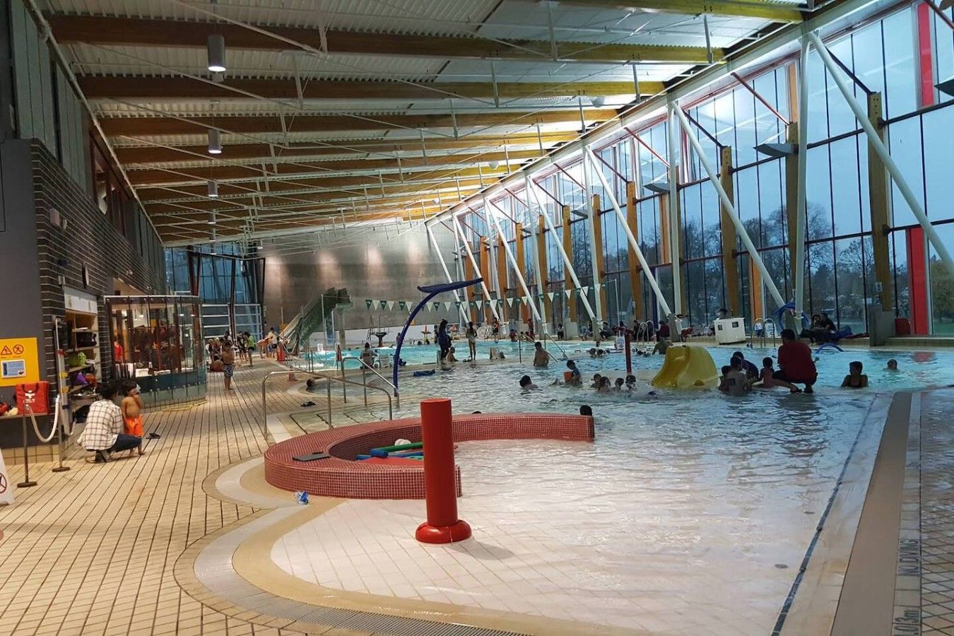 An indoor swimming pool with multiple lanes, a central play area, and a covered spectator area.