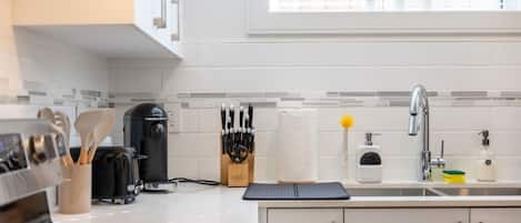 A modern kitchen with a coffee maker, knife set, and a window with blinds.