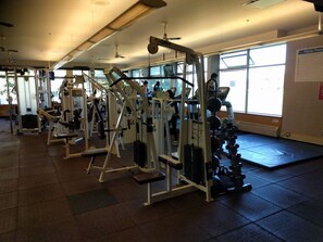 Une salle de sport équipée de divers appareils d’exercice, dotée de grandes fenêtres et d’un sol carrelé.
