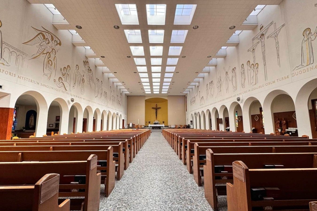 Ein Kircheninneres mit Holzbänken, einem zentralen Altar und religiöser Kunst an den Wänden.