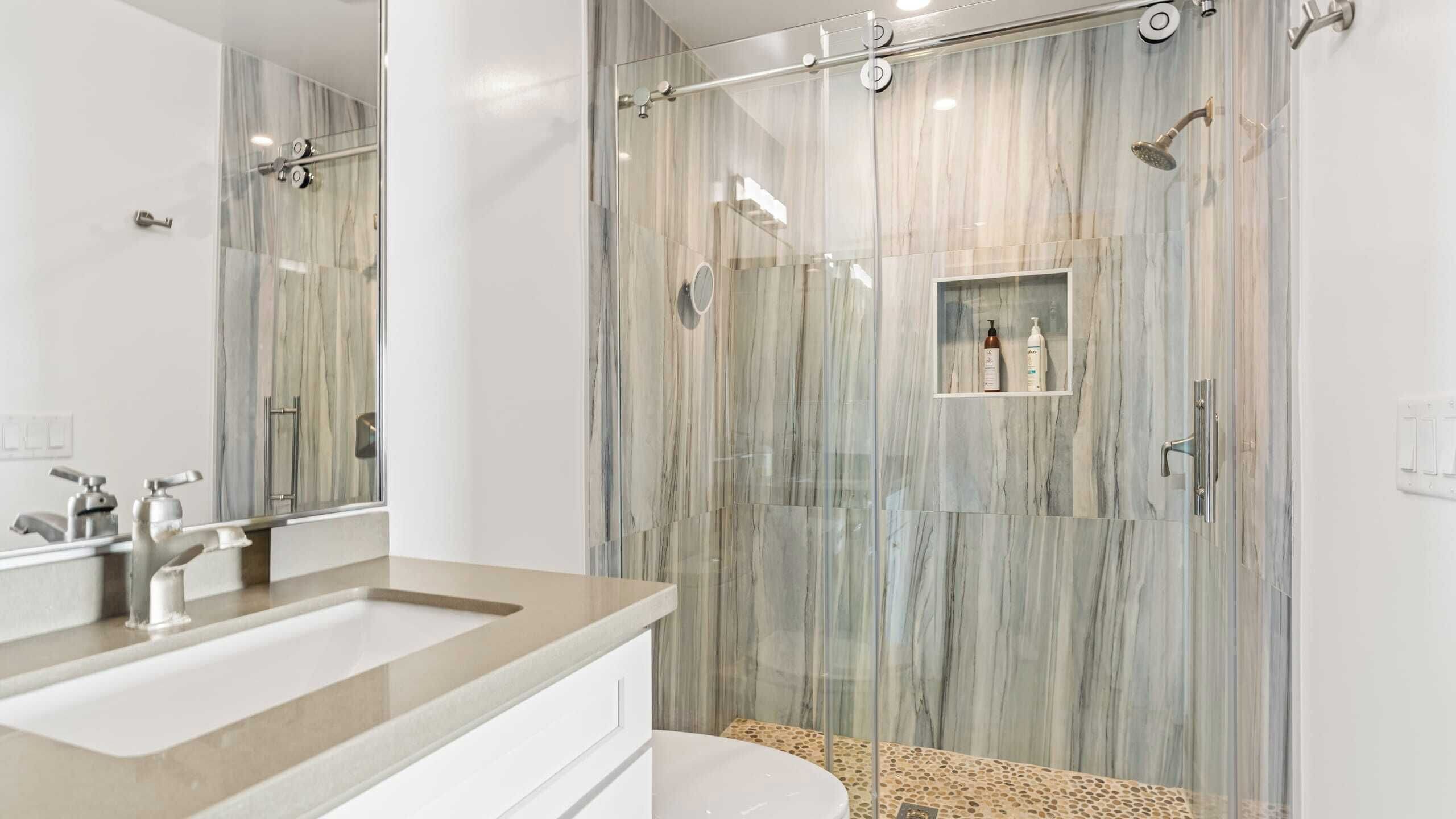 A modern bathroom with a marble shower enclosure, a vanity with a sink, and a toilet.