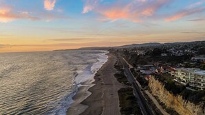 A coastal road with a beach on one side and residential buildings on the other. - Steps to Beach, Hot Tub + Private Patio 259 Trailhead Trestles 3 by Avantstay (San Clemente)