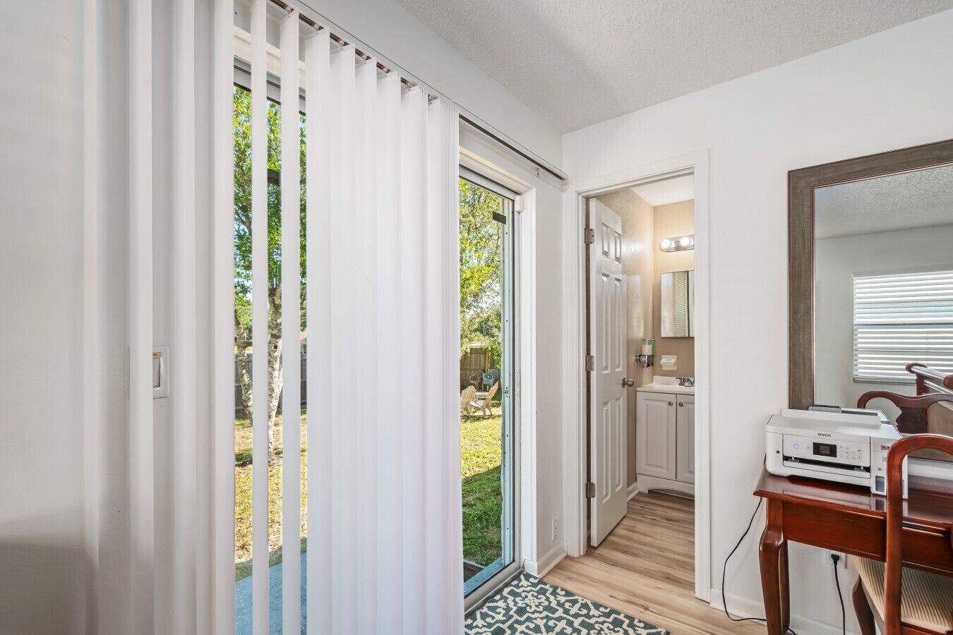 A modern bathroom with a shower, toilet, and sink. There is a mirror above the sink and a window with blinds.