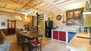 Une cuisine rustique avec un mur en pierre, un escalier en colimaçon en bois et un îlot de cuisine rouge et blanc.