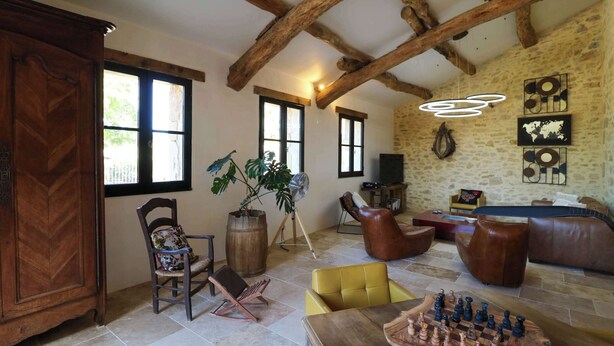 Un salon chaleureux avec une table basse en bois, un fauteuil jaune et un jeu d’échecs. On y trouve également des canapés en cuir et un meuble en bois.