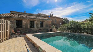 Un bâtiment en pierre doté d’une piscine, d’une terrasse avec des chaises et d’une clôture.