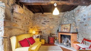 A rustic stone-walled room with a yellow sofa, a red chair, a fireplace, and a hanging light fixture. - Casa do Sarracas (Montalegre)