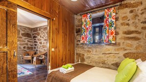 A cozy room with a stone wall, wooden ceiling, and a bed with green pillows. - Casa do Sarracas (Montalegre)