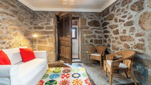 A cozy room with a white sofa, a wicker chair, and a colorful rug. - Casa do Sarracas (Montalegre)