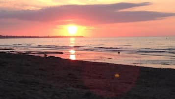 Een strand bij zonsondergang, met de zon laag aan de horizon, weerspiegeld in het water.