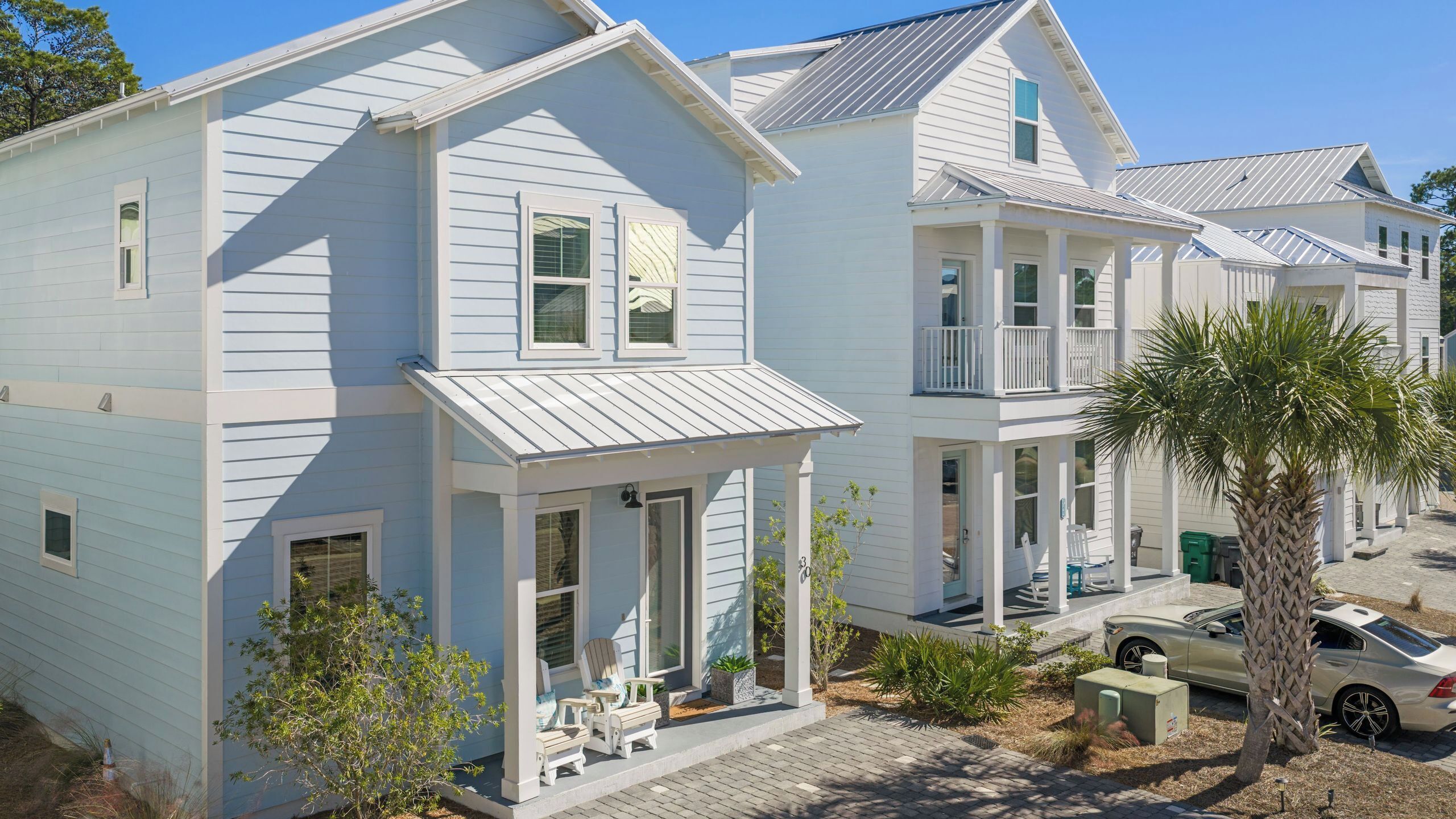 A two-story house with a covered porch, a car parked in front, and a palm tree.