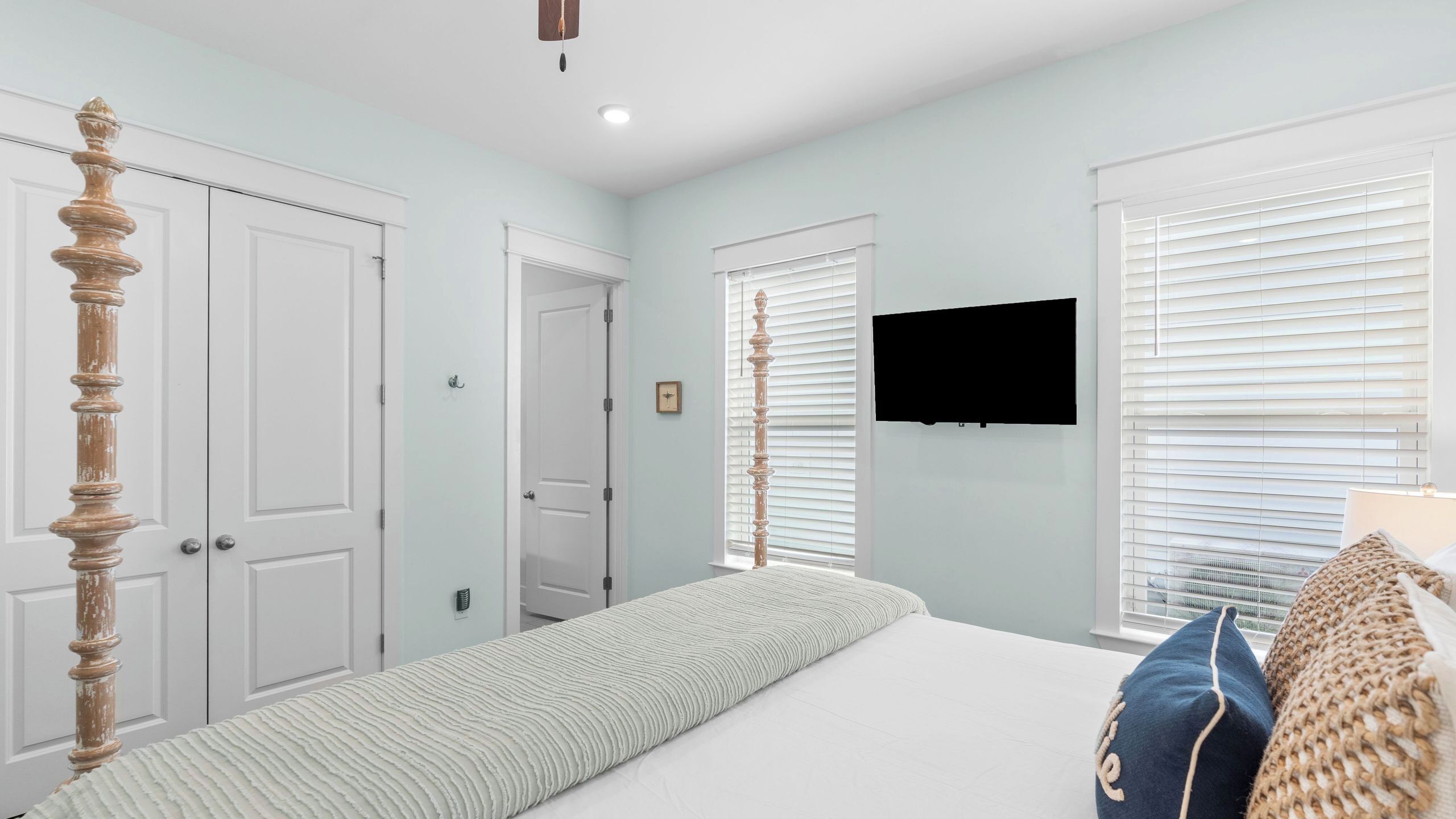 Une chambre à coucher avec un lit à baldaquin, un téléviseur à écran plat fixé au mur et une fenêtre avec des stores.