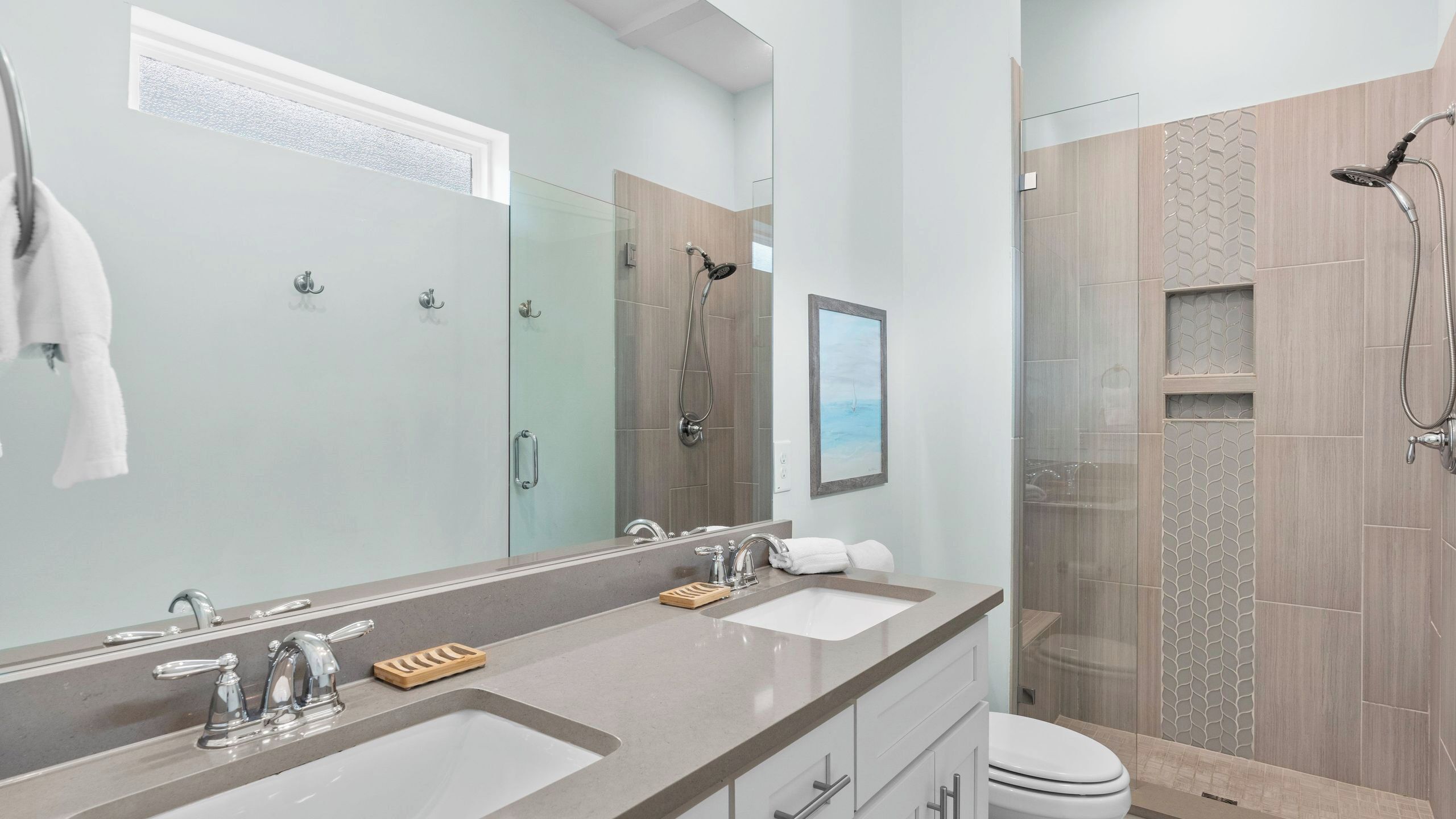 A modern bathroom with a large mirror, two sinks, a shower, and a toilet.