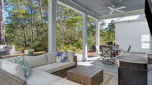 An outdoor patio with a sofa, dining table, chairs, and a grill area. - Constant Getaway by Avantstay 30A Coastal Retreat Outdoor Lounge, Golf Cart, Bikes + Near Beach (Santa Rosa Beach)