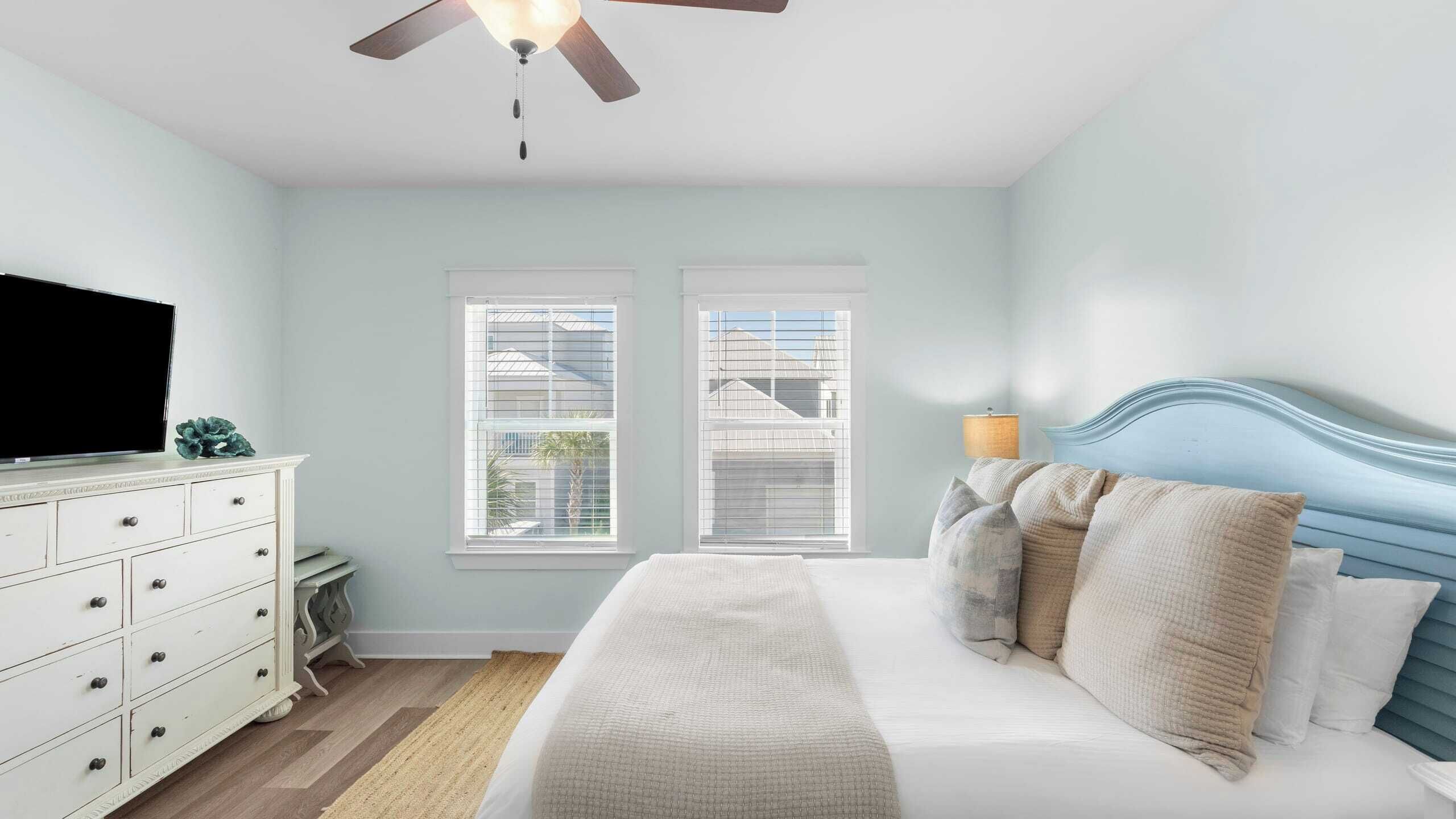 A bedroom with a bed, dresser, TV, and windows.