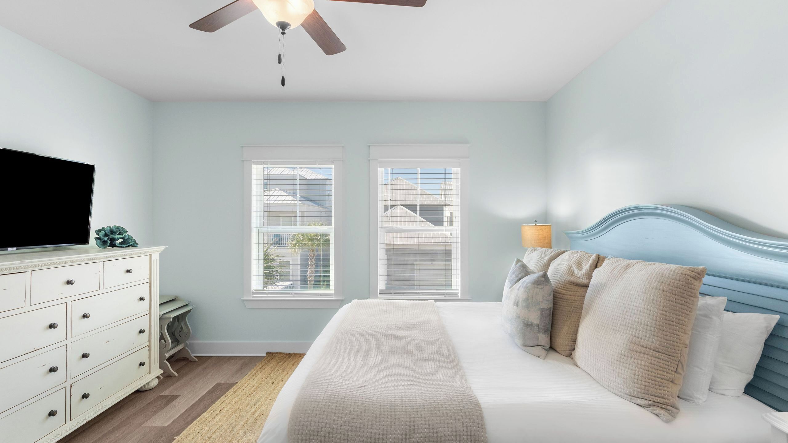 A bedroom with a bed, dresser, TV, windows, and ceiling fan.