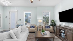 A living room with a sofa, two armchairs, a coffee table, a TV, and a cabinet. - Constant Getaway by Avantstay 30A Coastal Retreat Outdoor Lounge, Golf Cart, Bikes + Near Beach (Santa Rosa Beach)