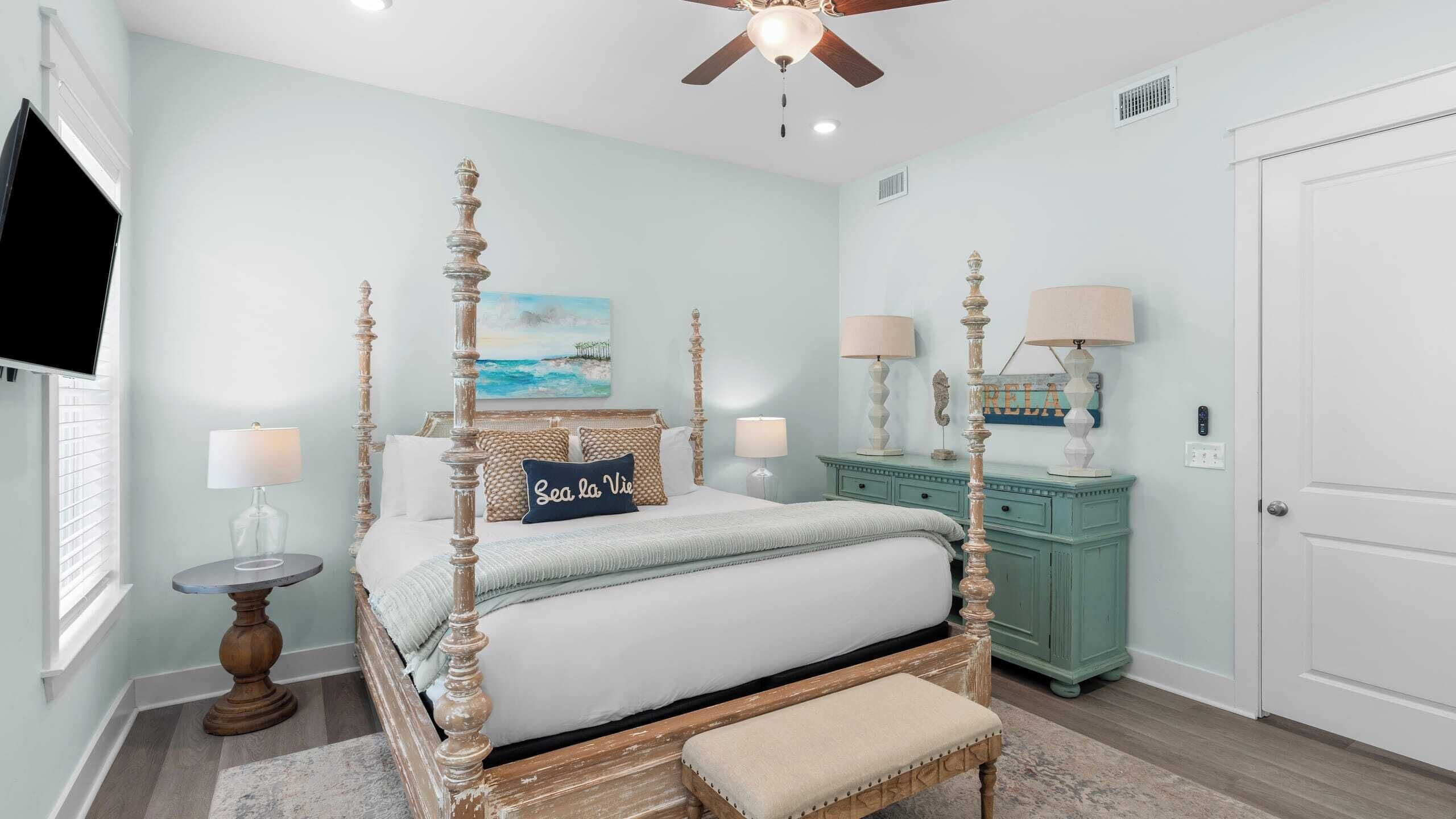 Un dormitorio con cama con dosel, un cuadro en la pared, una mesita de noche, un aparador y un ventilador de techo.