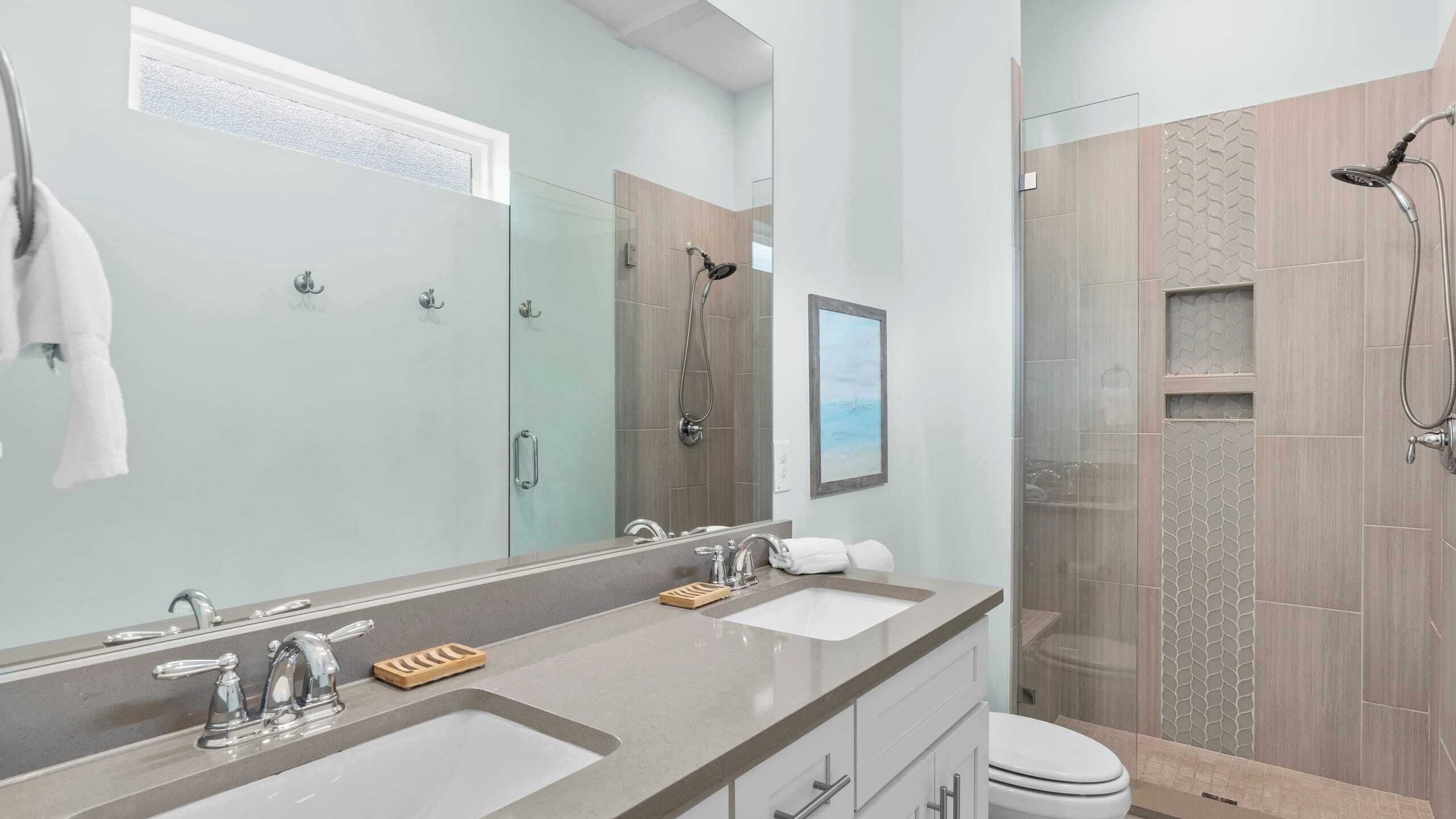 A modern bathroom with a large mirror, two sinks, a shower, and a toilet.