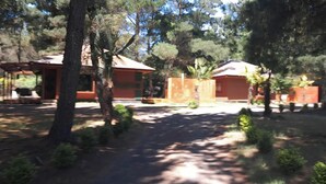 A rustic cabin-style building with a brick exterior and a thatched roof, surrounded by dense trees and a well-maintained garden.