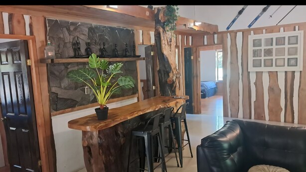 A rustic interior with a wooden bar, black stools, a black leather sofa, and a plant.