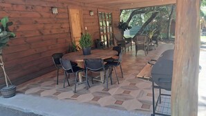 A wooden cabin with a covered patio featuring a round table and chairs, a grill, and potted plants.