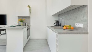 Una cucina moderna con mobili bianchi, un piano di lavoro grigio e una piccola isola. C'è un lavello con un rubinetto, una macchina per il caffè e una ciotola di frutta sul piano di lavoro.