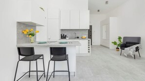 Una cucina moderna con mobili bianchi, un piano di lavoro grigio e due sgabelli neri.