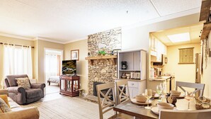 A cozy living room with a stone fireplace, comfortable seating, and a dining area set for a meal. - 10 Minutes Walk To Anakeesta, 2BR/2BA, Sleeps 6, Elevator on Premises (Gatlinburg)