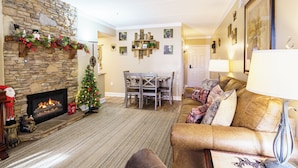 A living room with a stone fireplace, a Christmas tree, a dining area, and a sofa with a lamp. - 10 Minutes Walk To Anakeesta, 2BR/2BA, Sleeps 6, Elevator on Premises (Gatlinburg)