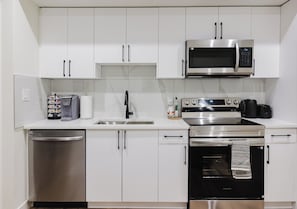 A modern kitchen with white cabinets, a stainless steel dishwasher, a microwave, a stove, and an oven.
