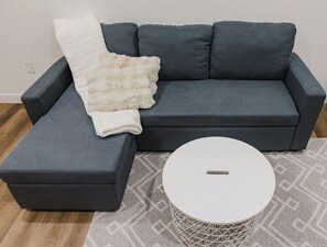 A grey sofa with a white throw blanket and a white coffee table with a woven base.