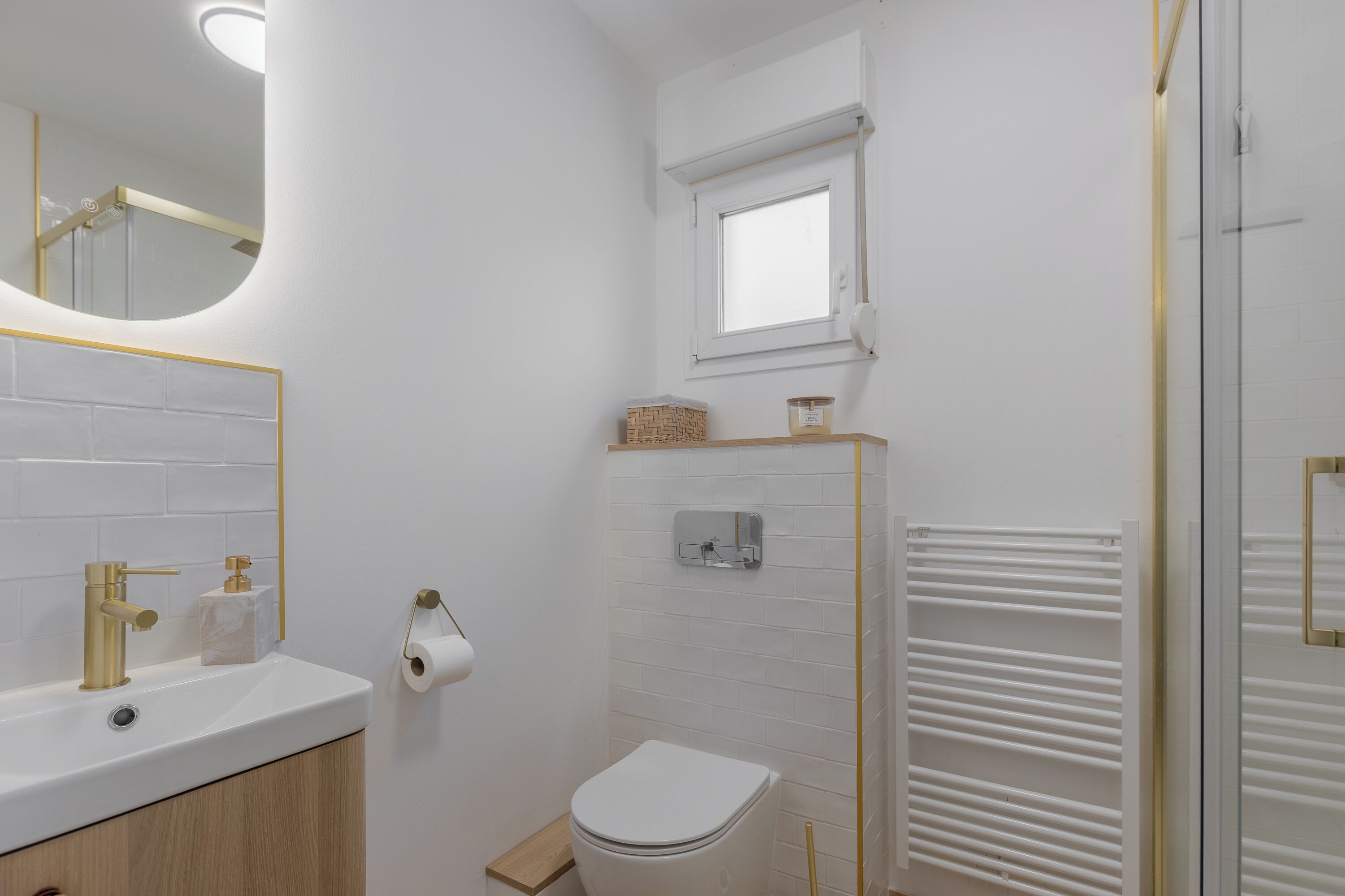 Ein Badezimmer mit weißem Waschbecken, goldenen Armaturen, einer Toilette, einem Fenster und einem Handtuchhalter.