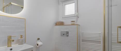 Ein Badezimmer mit weißem Waschbecken, goldenen Armaturen, einer Toilette, einem Fenster und einem Handtuchhalter.