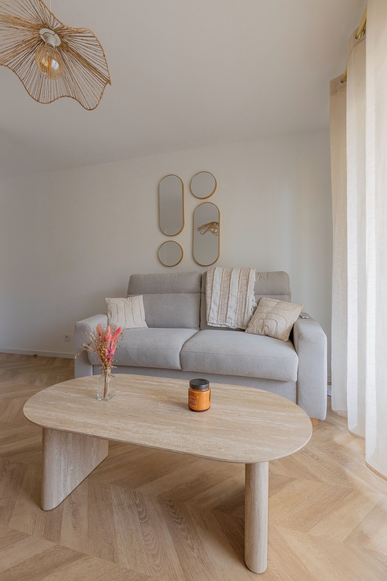 A minimalist living room with a grey sofa, a round coffee table, and a hanging light fixture.