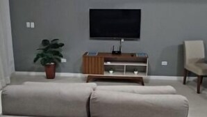 Ein Wohnzimmer mit einem großen, beigefarbenen Sofa, einem flachbildfernseher an der Wand, einer Holzunterhaltungsecke und einem Deckenventilator.
