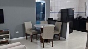 Ein modernes Wohnzimmer mit Sofa, Esstisch, Stühlen, einer Küchenzeile mit Kühlschrank und Schränken sowie einem großen Fenster für natürliches Licht.